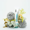 Minimalist product shot of a hydrating K-beauty cream tube placed among soft, neutral-toned flowers and greenery, creating a fresh, clean skincare aesthetic.