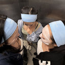 Overhead view of three friends wearing blue Baerry headbands and sheet masks, standing together in an elevator, capturing a fun, casual K-beauty skincare moment.