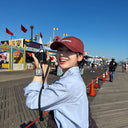 Young Asian woman with glowing K-beauty skin smiling outdoors on a sunny Coney Island boardwalk — daily SPF for outdoor activities