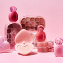 Assorted pink-toned K-beauty makeup products, including lip tints, eyeshadow palettes, and heart-shaped packaging, arranged on a soft pink background for a playful, glossy aesthetic.