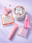 A flat-lay arrangement of six beauty products on a light lavender background: a pink nail polish bottle and applicator, a tray of false eyelashes, a white jar of heimish All Clean Balm, a pink tube, a pink pump bottle of numbuzin, and a two-pan makeup palette.